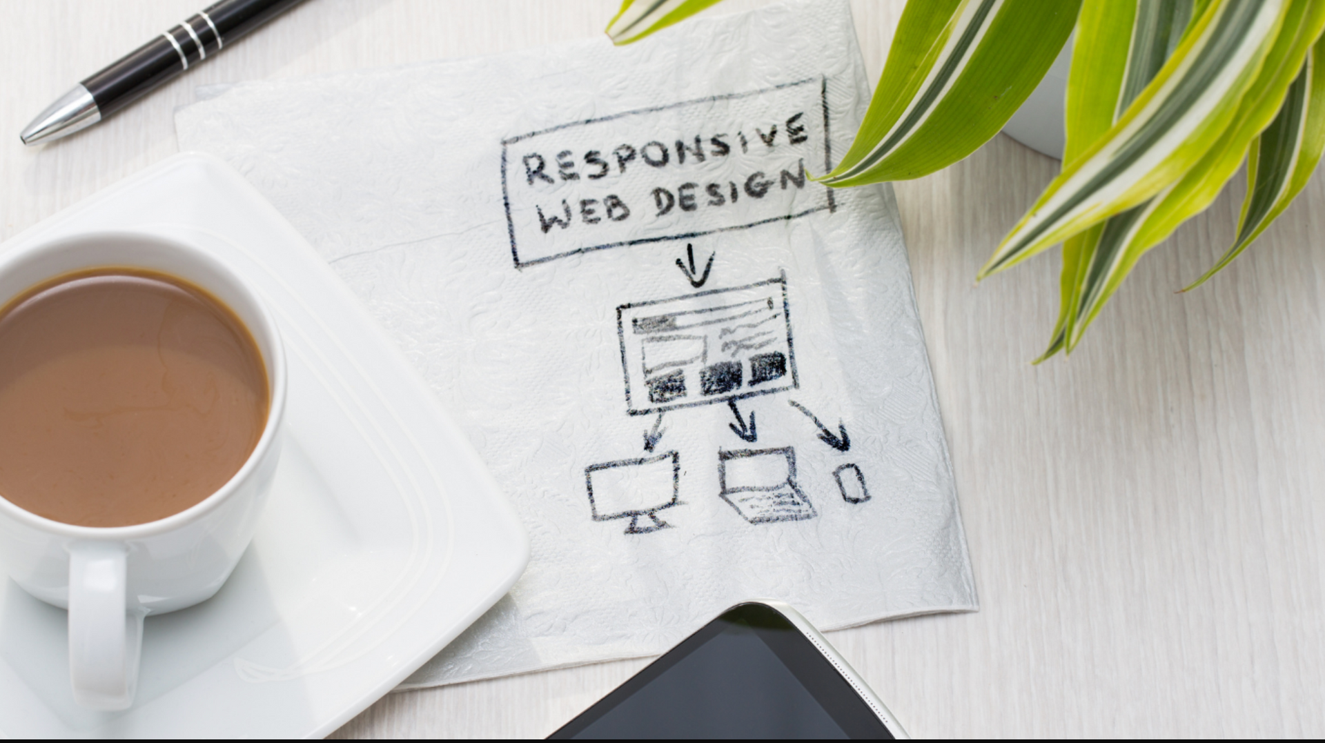 A cup of coffee , a pen , a cell phone , and a napkin with responsive web design written on it.