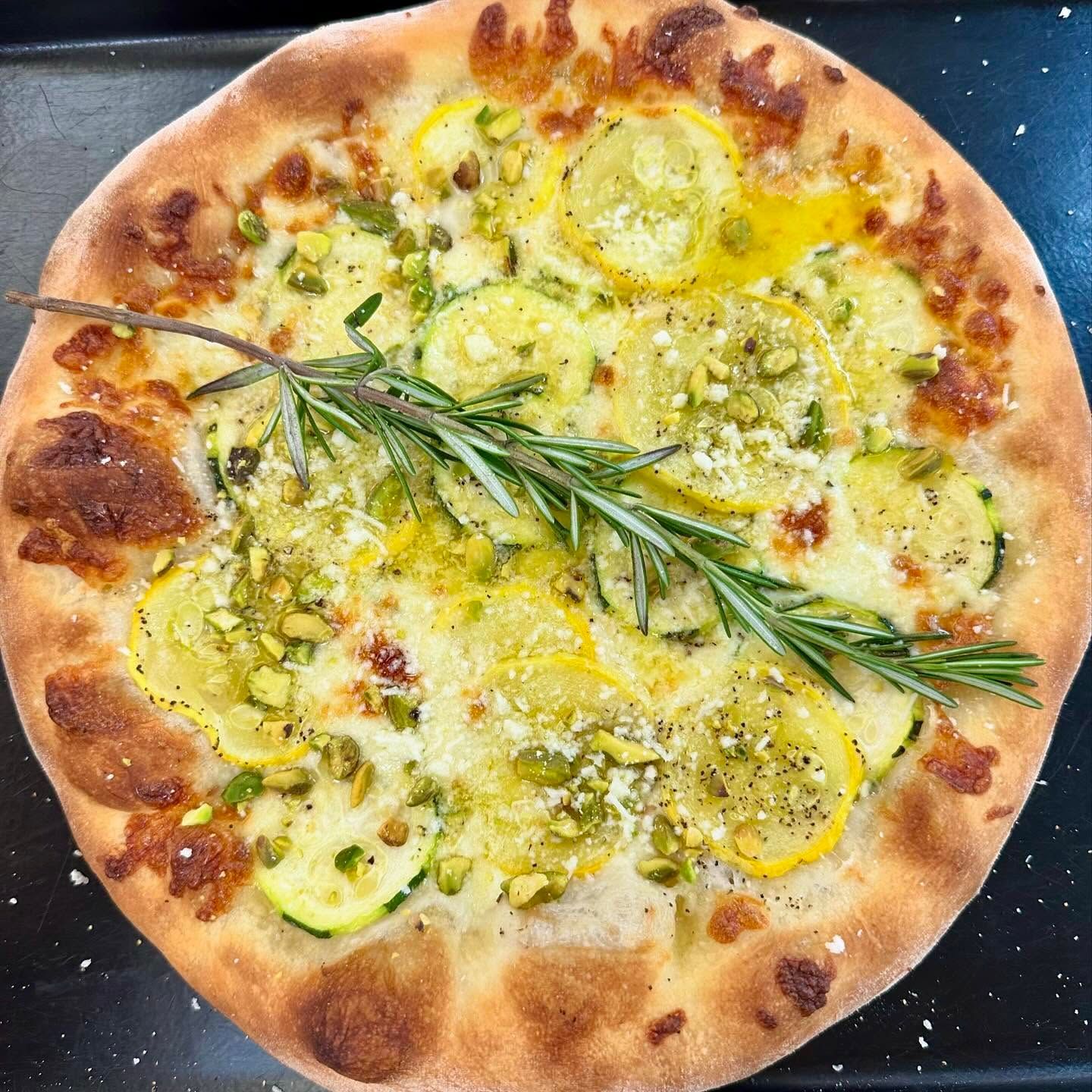 A pizza with a sprig of rosemary on top is sitting on a pan.