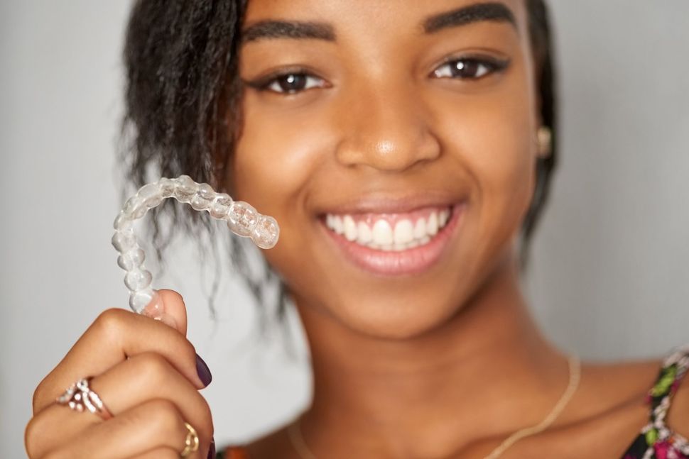 A young woman is smiling while holding a clear retainer in her hand.