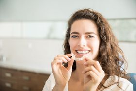A woman is holding a aligners in front of her mouth.