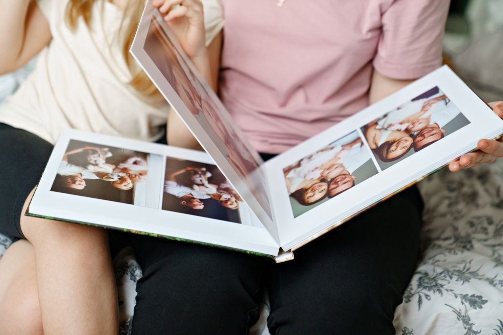 People sitting on a bed, looking at a photo album with multiple photos.