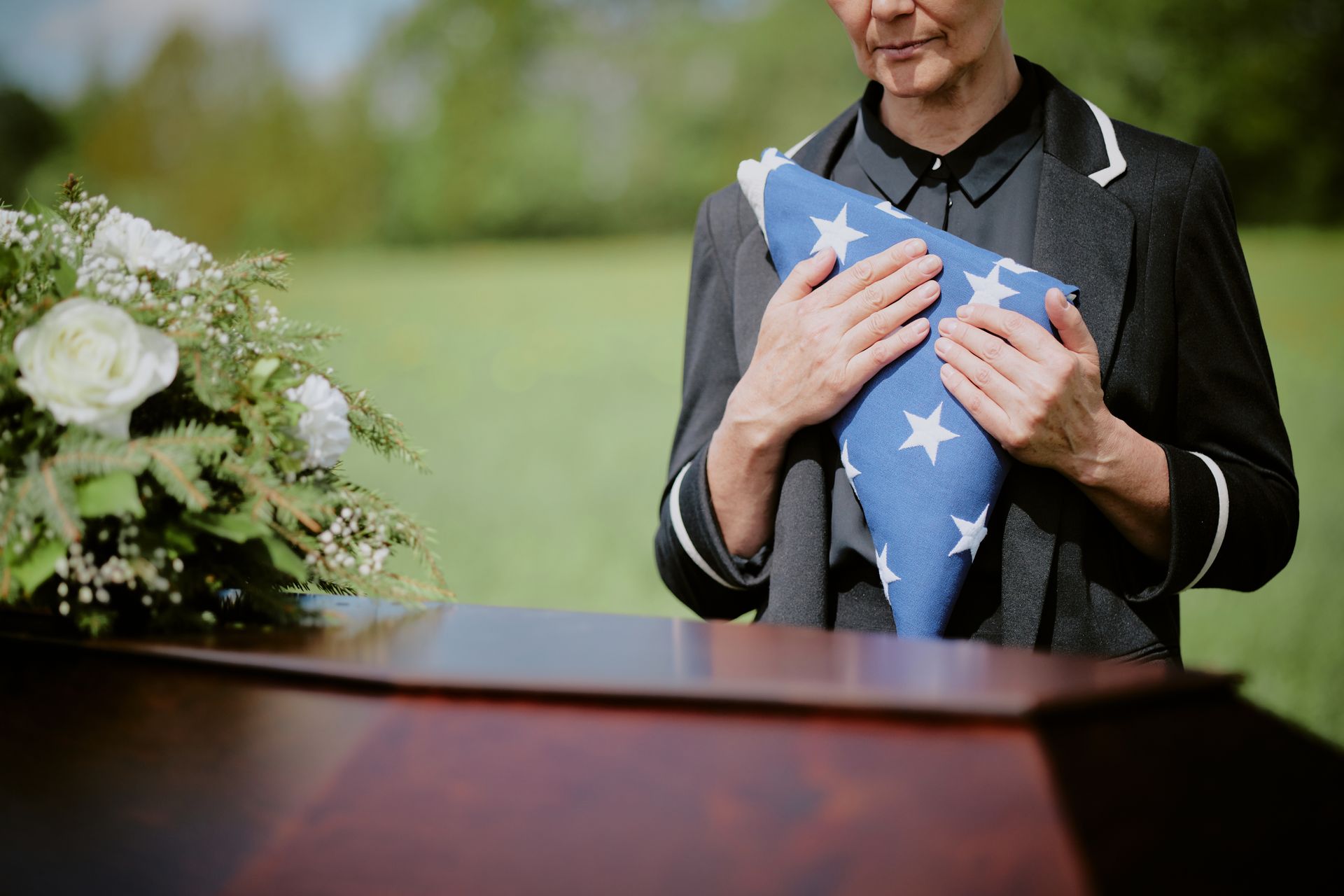 Woman holding a folded American flag and a rose at a funeral.