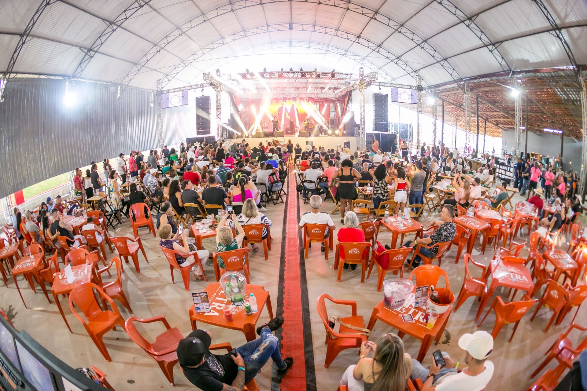 Um grande grupo de pessoas está sentado em mesas e cadeiras em uma sala grande.