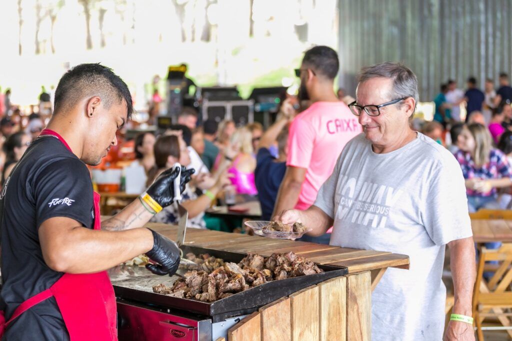 Um homem está cozinhando comida em uma grelha na frente de uma multidão de pessoas.