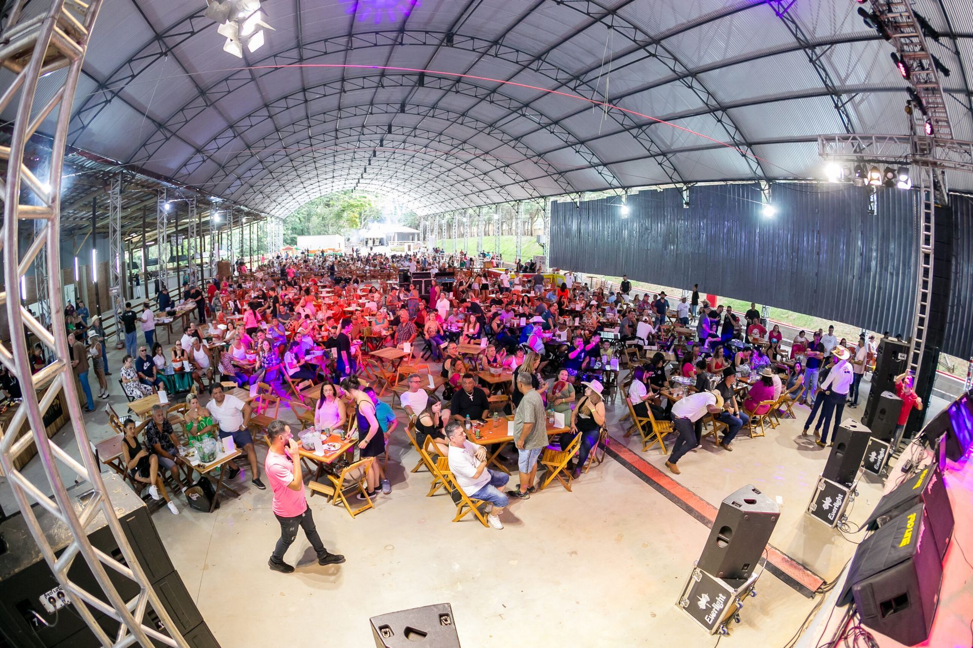 Um grande grupo de pessoas está sentado em mesas sob uma tenda.