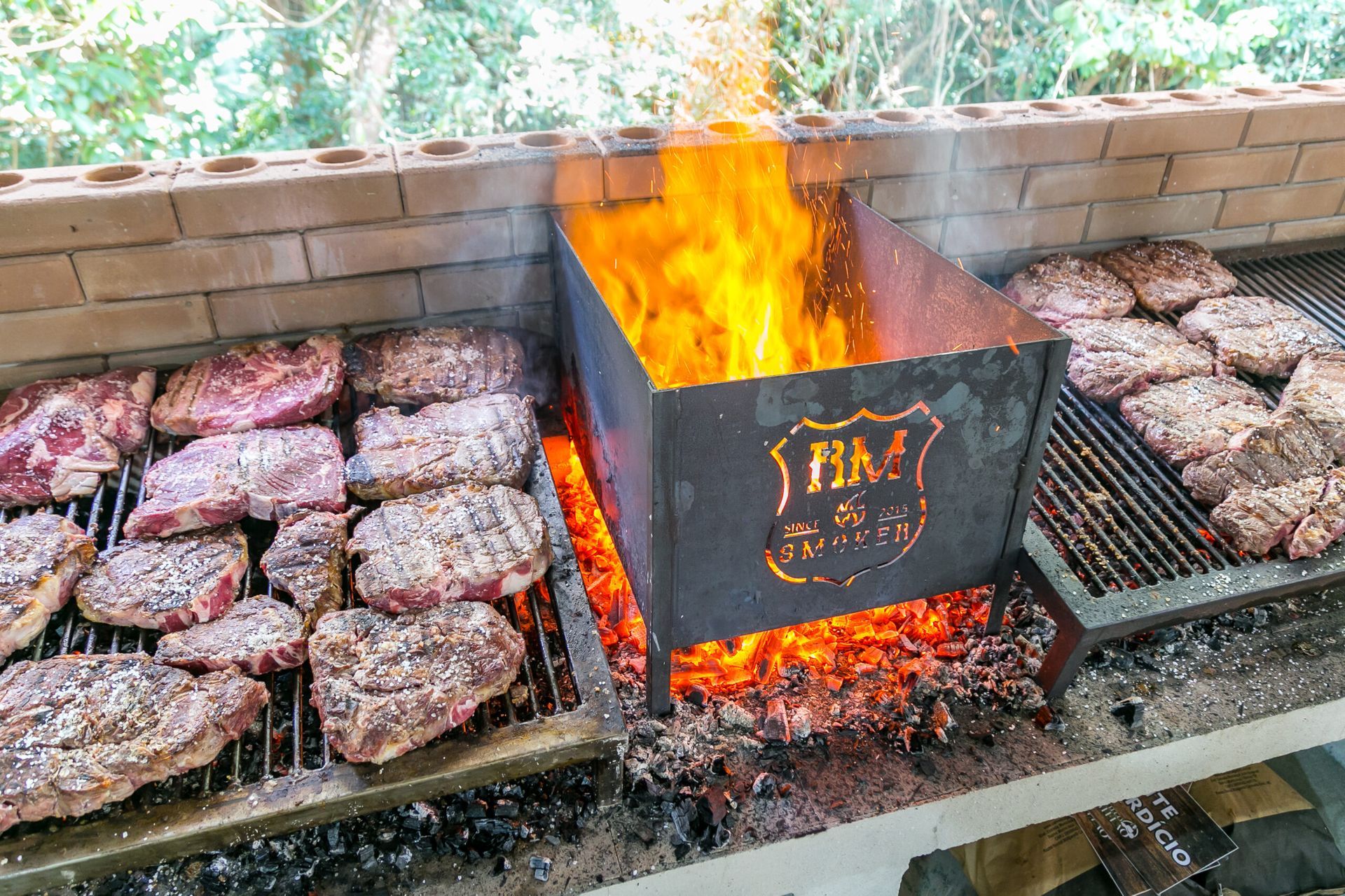Uma grelha cheia de carne e hambúrgueres está cozinhando no fogo.