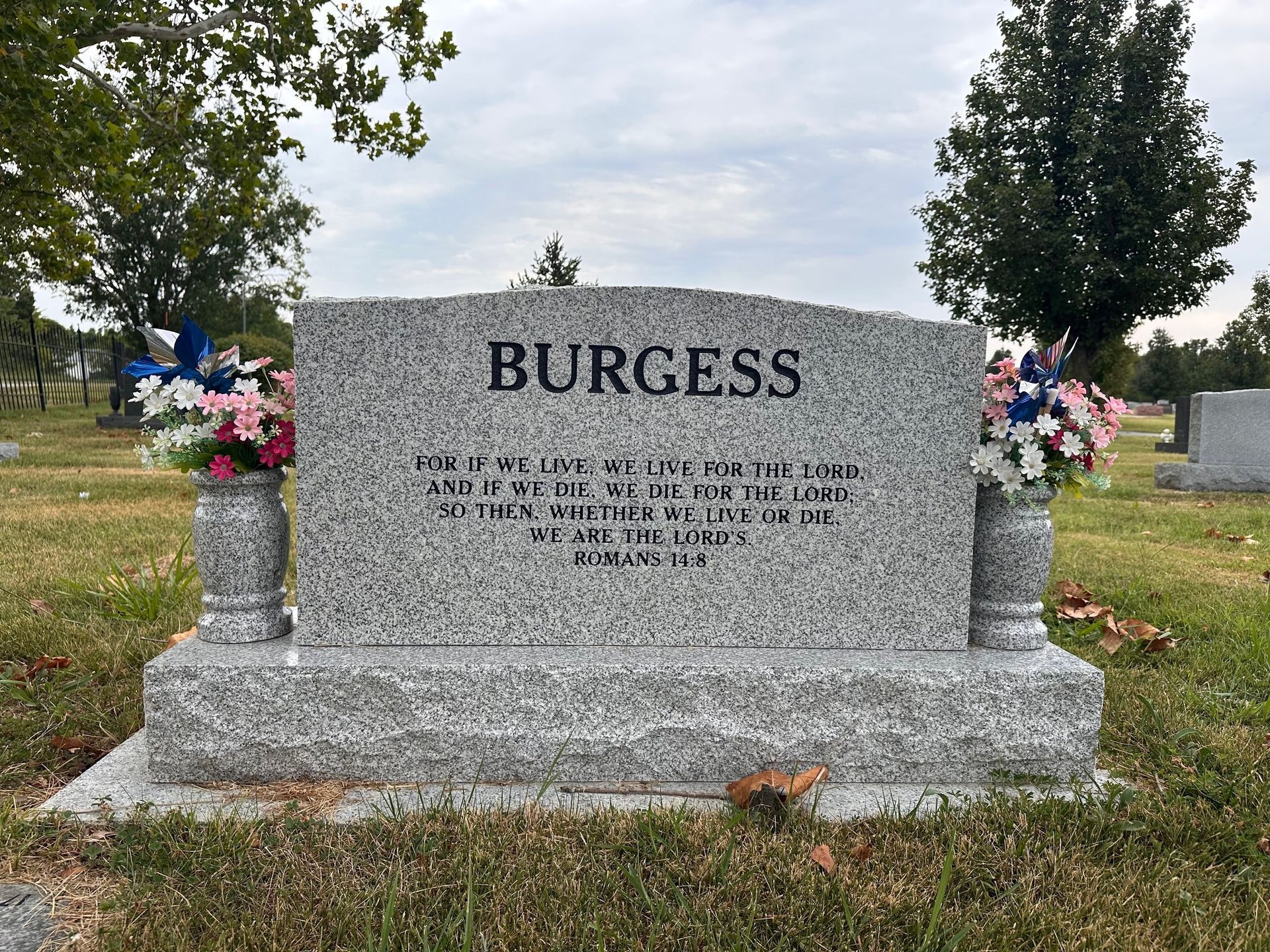 Gravestone of the Burgess family at a cemetery, with floral decorations on either side.