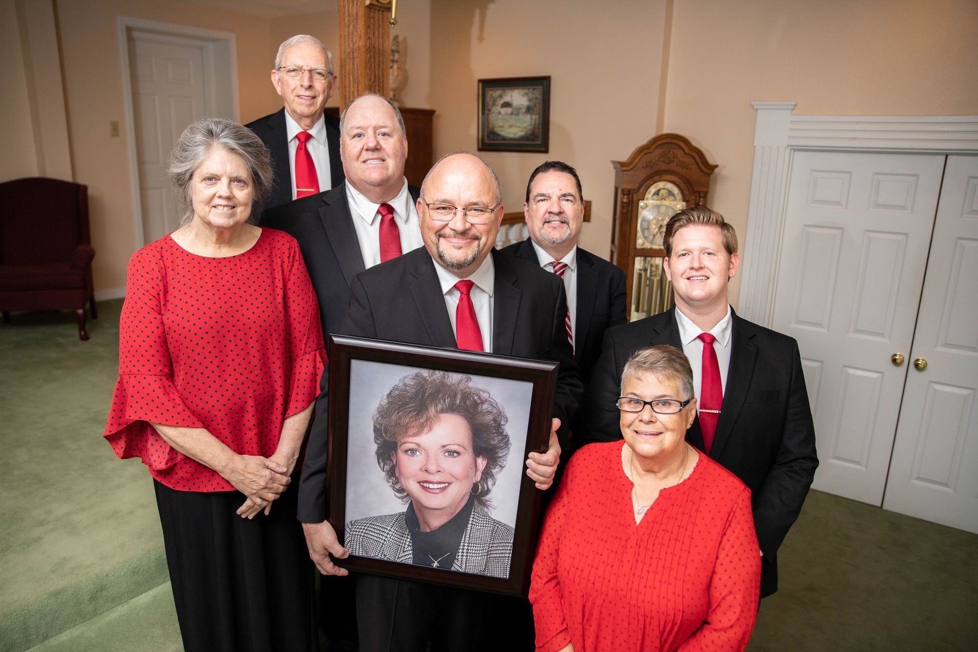 A group of people standing around a man holding a picture of a woman.