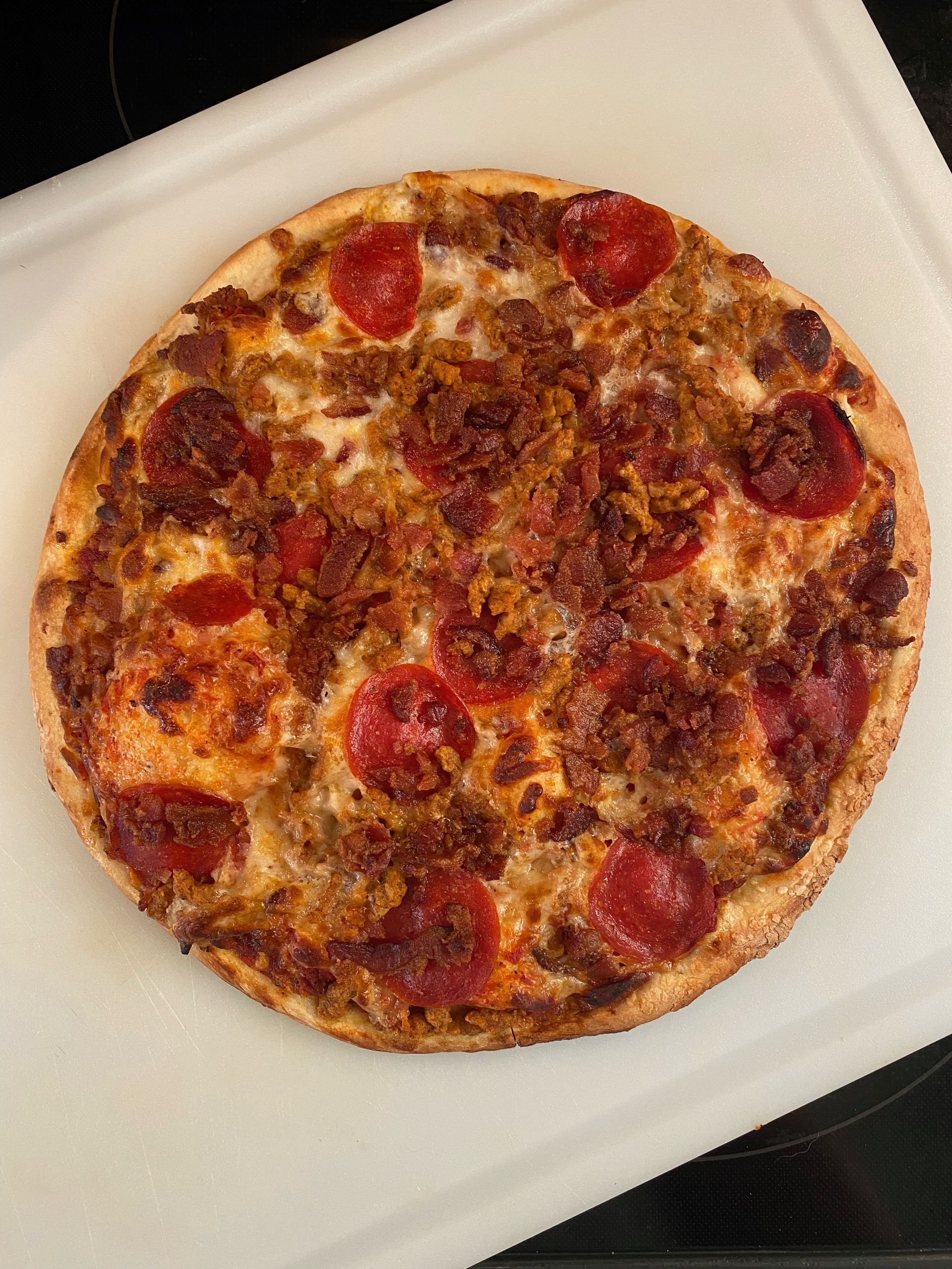 A round pizza with pepperoni and sausage on a white cutting board.