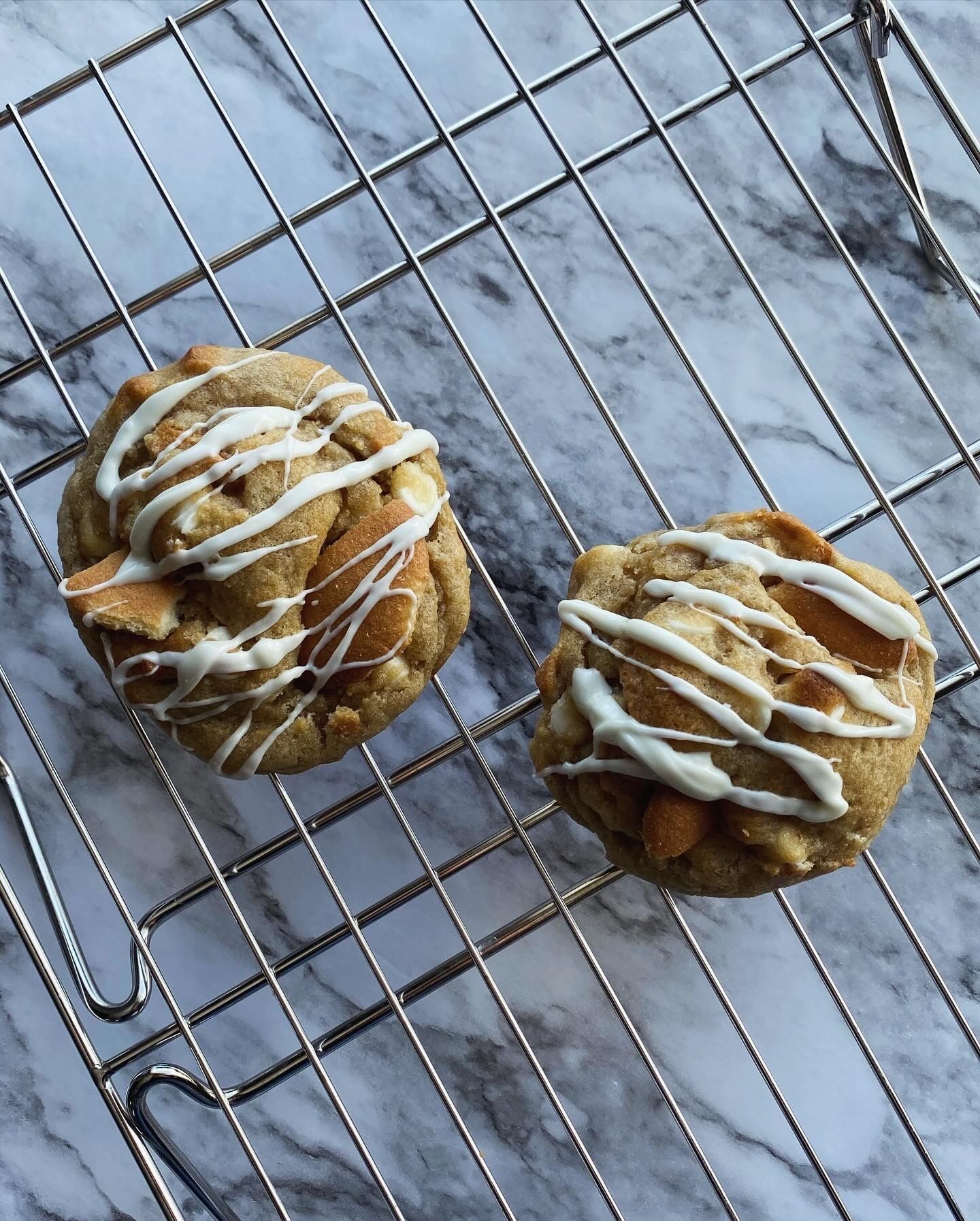 Two cookies on a wire rack, drizzled with white icing, and topped with almond slices, against a marble surface.