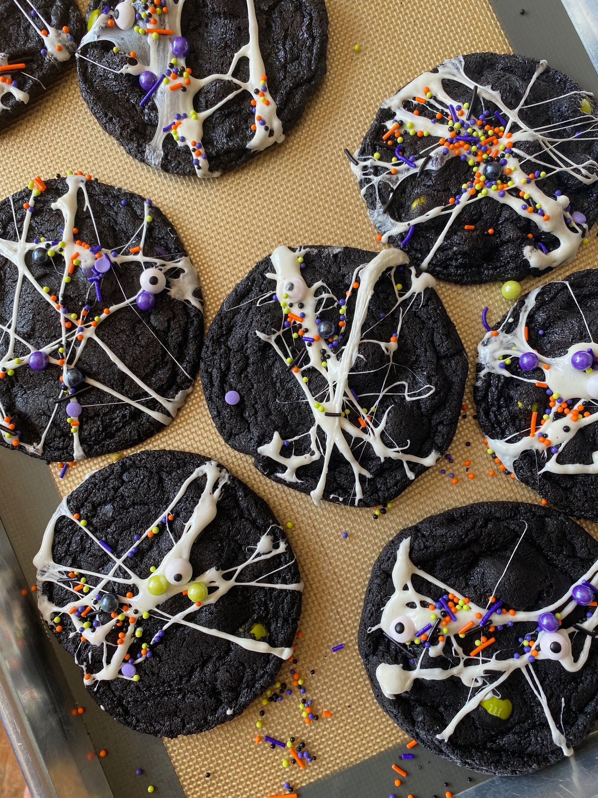 Black Halloween cookies drizzled with white icing, sprinkles, and