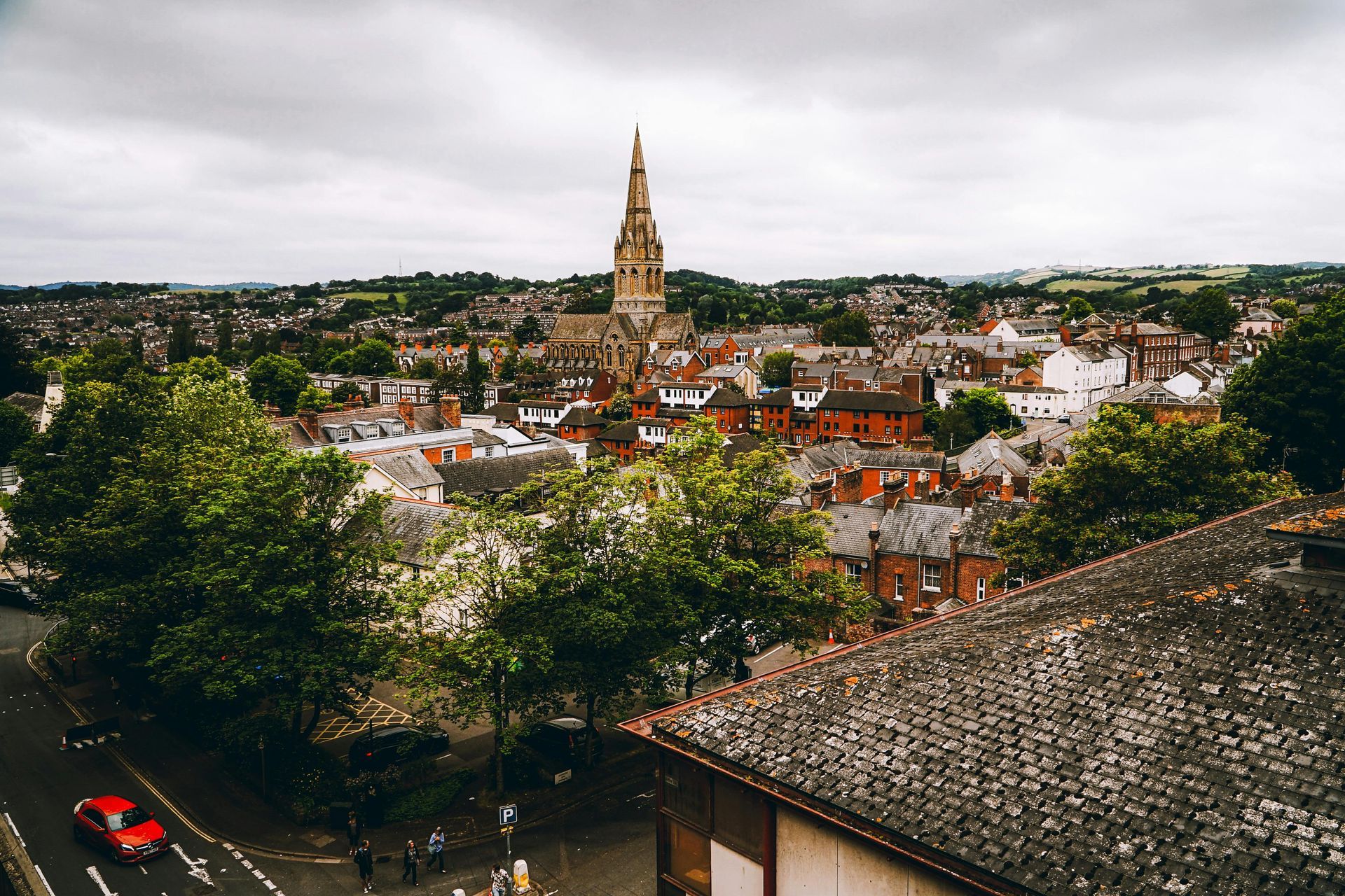 Town skyline with a tall church spire above red-roofed buildings, viewed from a hillside overlook