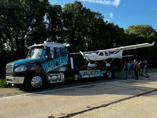 A tow truck is carrying a small plane on the back of it.