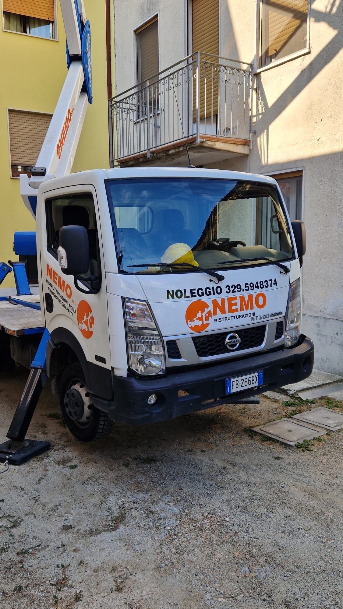 Camion bianco con piattaforma aerea, parcheggiato sul selciato. Scritta