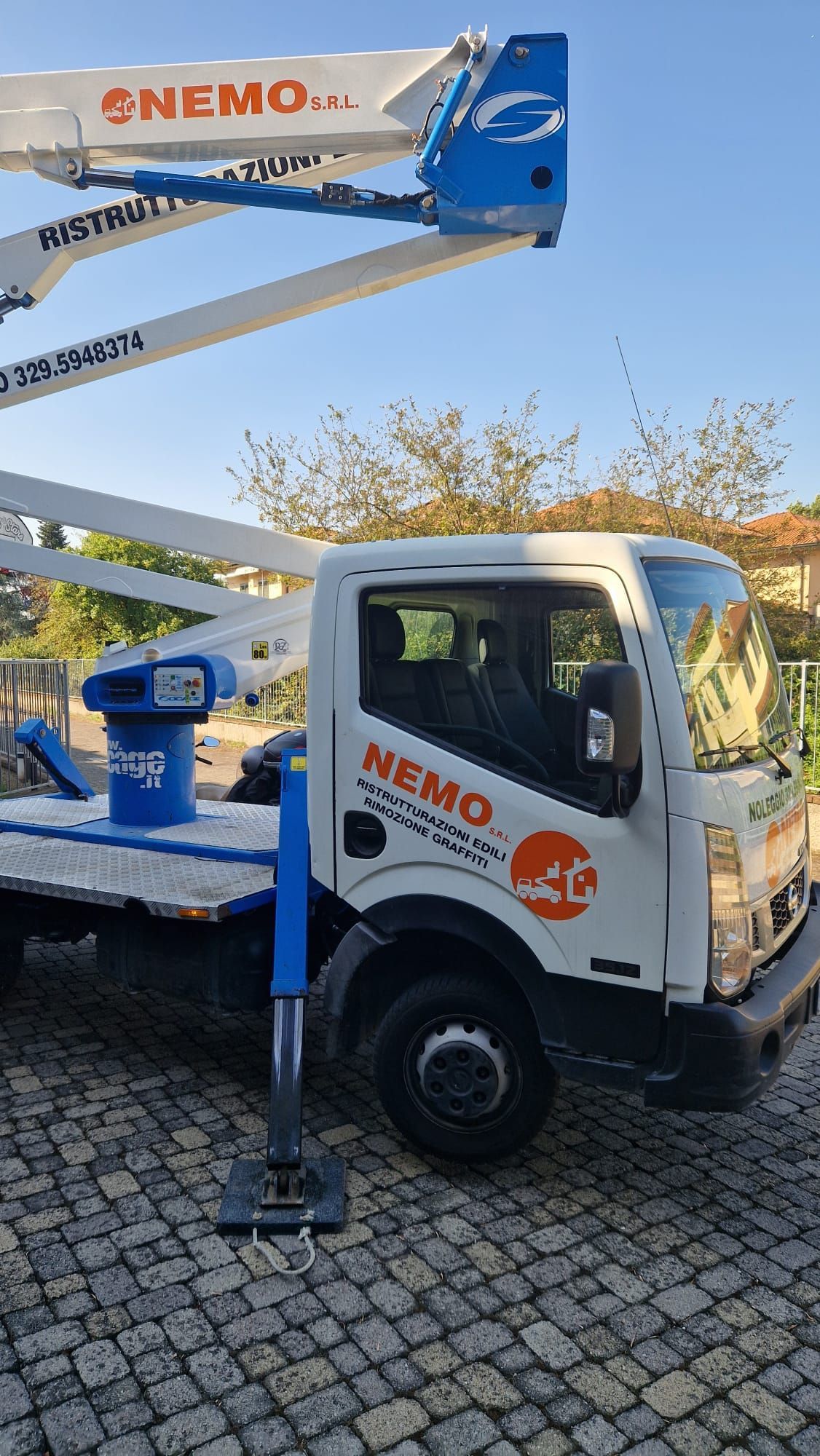 Camion Nemo bianco con sollevatore rialzato in un'area asfaltata, accanto al verde, contro un cielo azzurro.