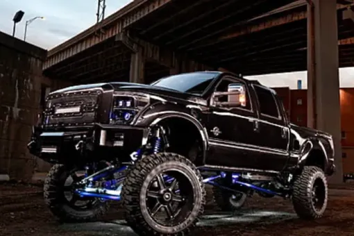 Black lifted truck with large tires and blue underglow, parked beneath an overpass.