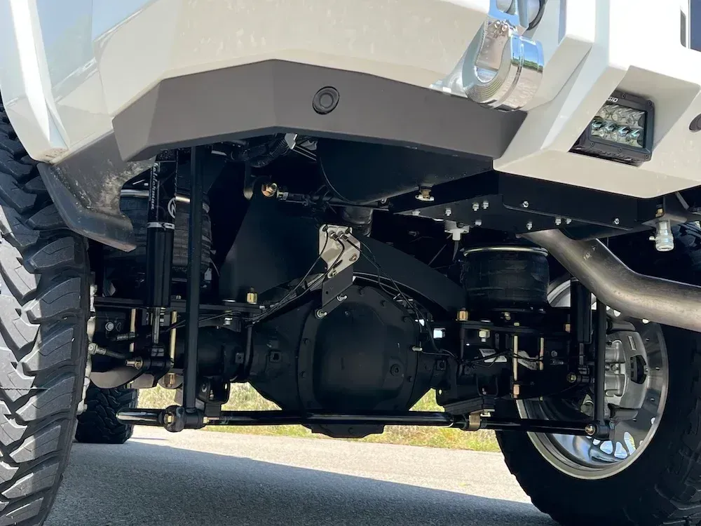 Rear suspension of a lifted truck with black components and large tires on pavement.