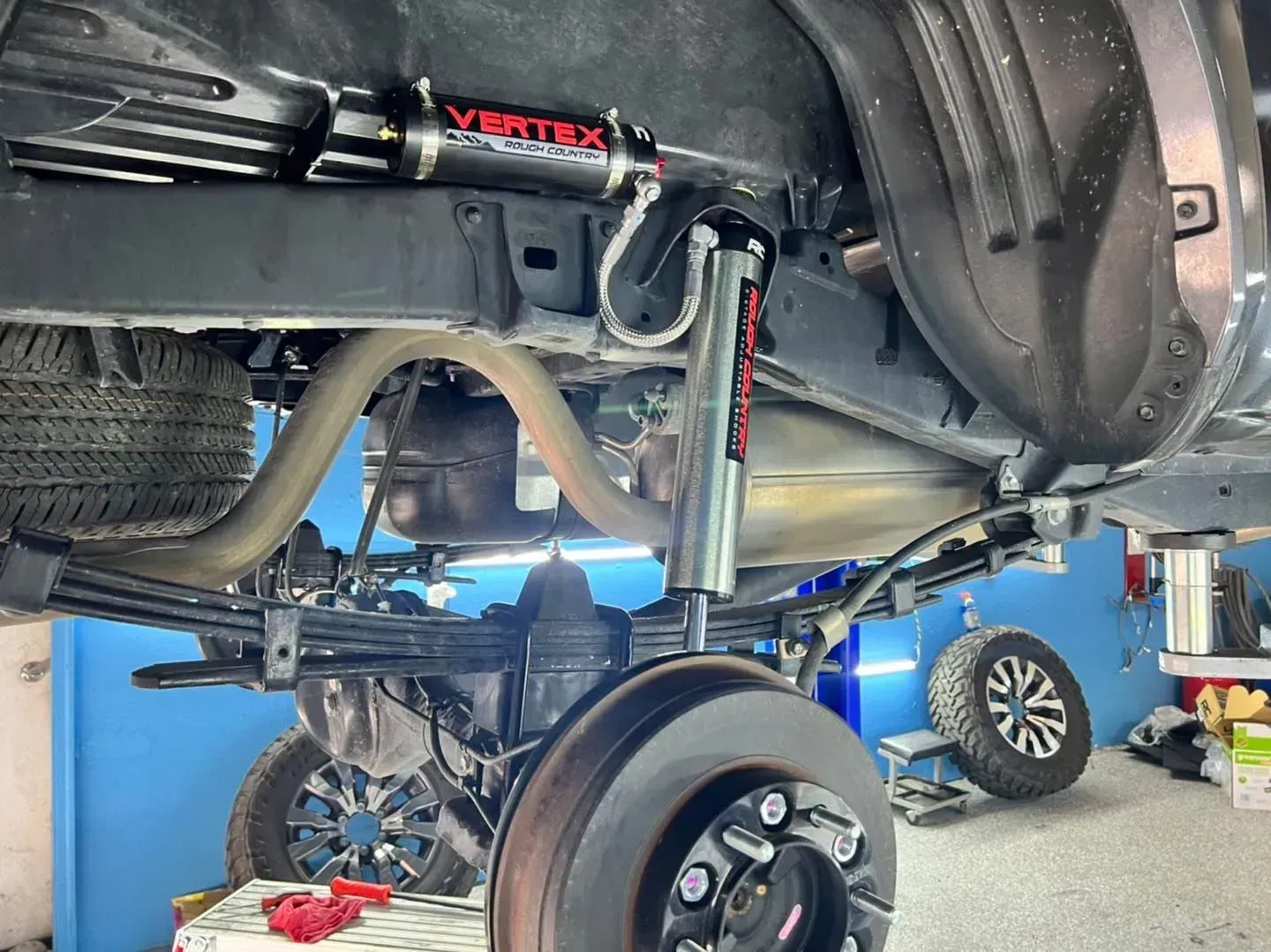 Rear underside of a truck with installed Vertex suspension, showcasing the shocks and components in a shop setting.