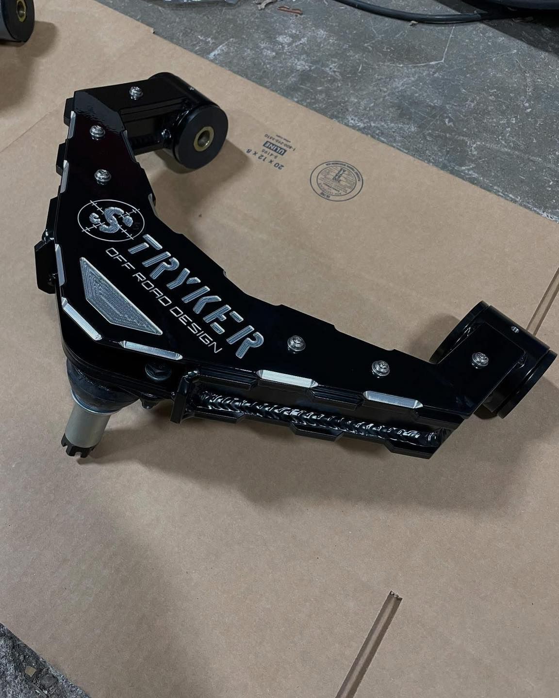 Black Stryker Off Road Design upper control arm on cardboard.