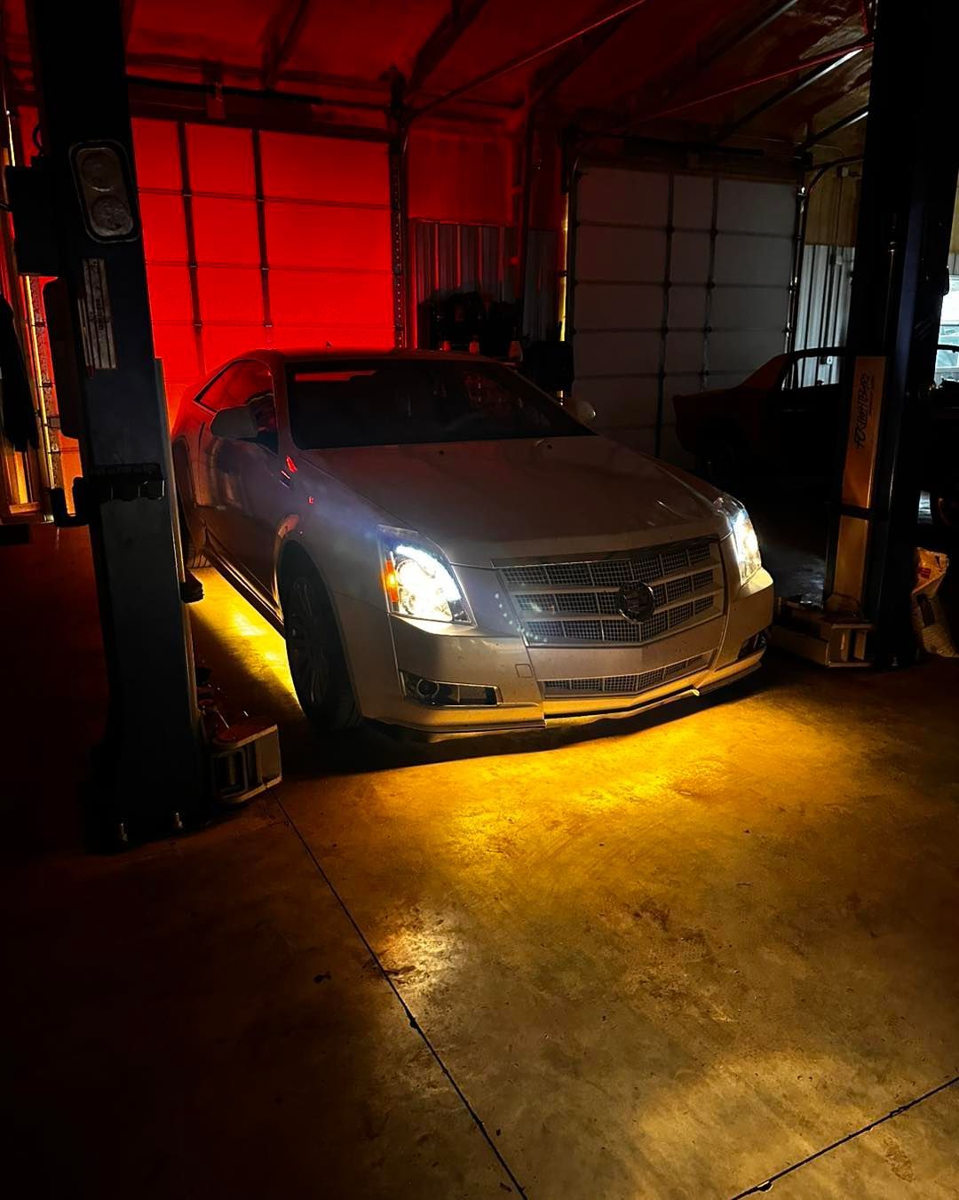 Silver car in a garage with yellow lights, red background, standing on a concrete floor.