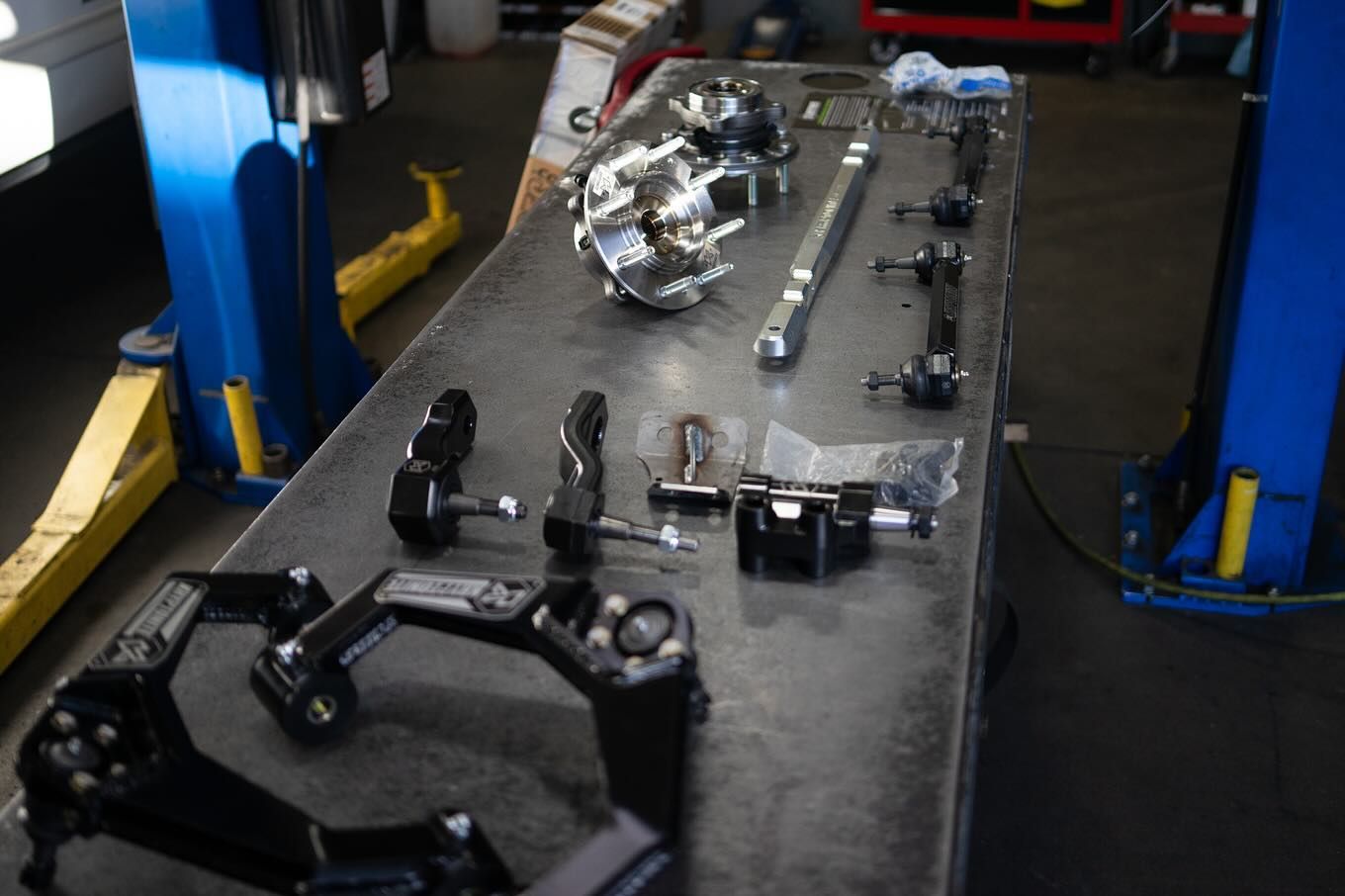 Car parts on a workbench in a garage. Black, silver, and blue components scattered for assembly.