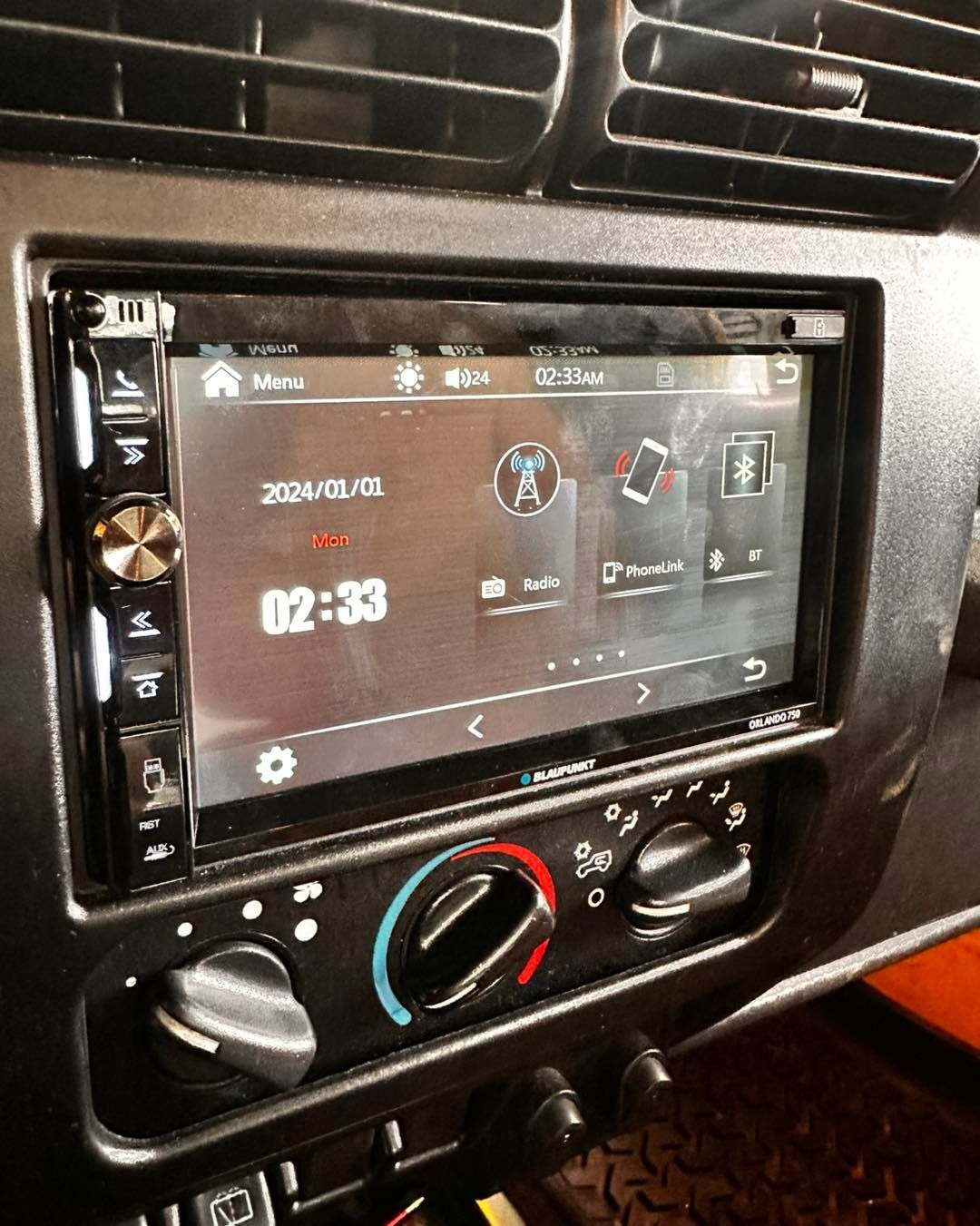 Car dashboard with a touchscreen radio displaying a clock and icons. Black panel, air vents, and controls.