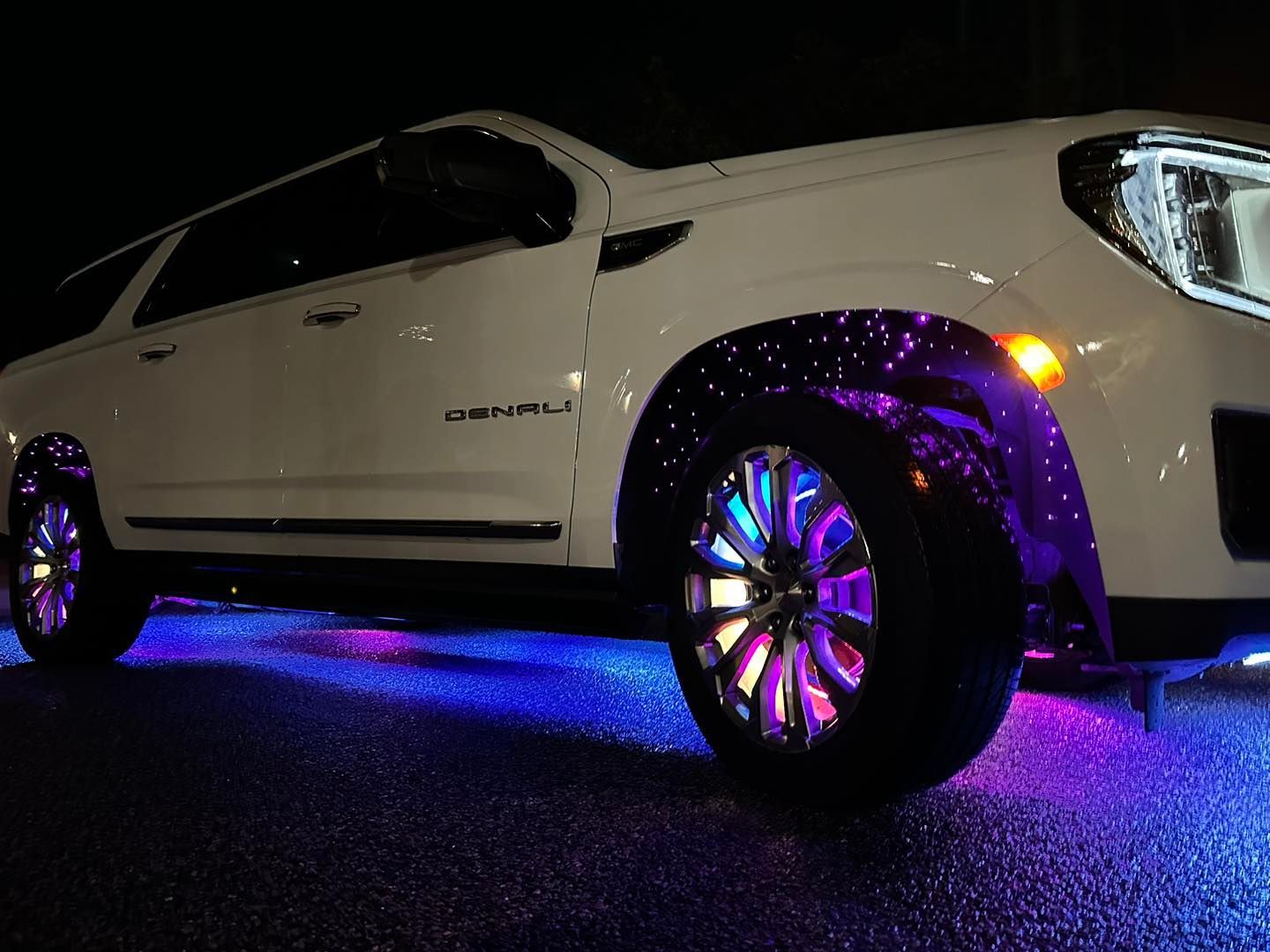 White SUV with purple wheel well and blue underglow lights at night.