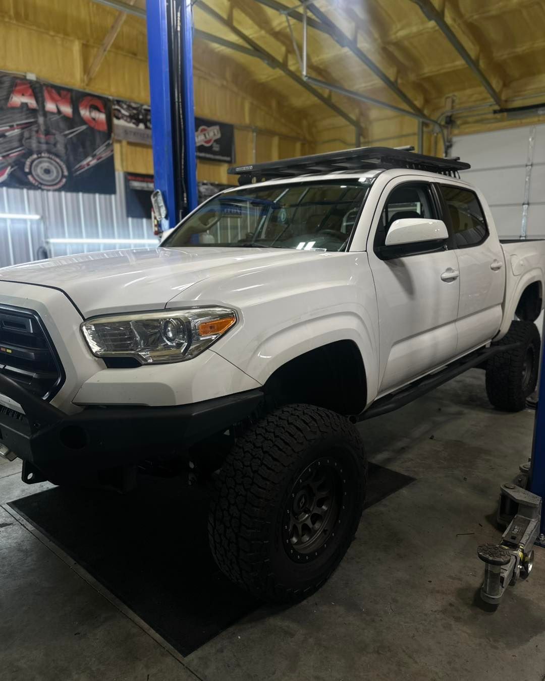 White lifted Toyota Tacoma truck in a garage, with a roof rack and large tires.