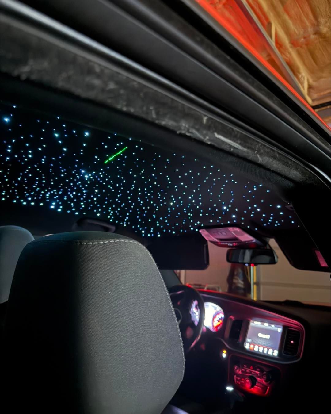 Black car interior with starry ceiling lights, a seat, dashboard, and red accents.