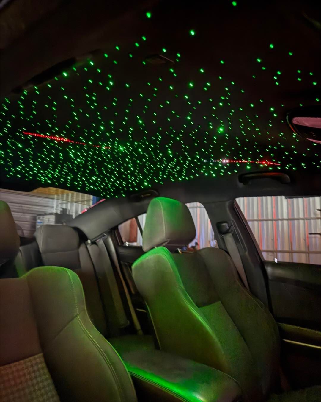 Green starry ceiling in a car, illuminated interior. Gray seats are visible.