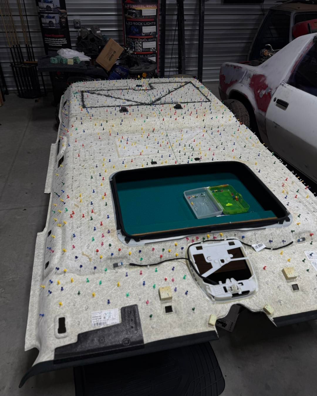 Car ceiling panel with sunroof opening, covered in insulation, in a garage.