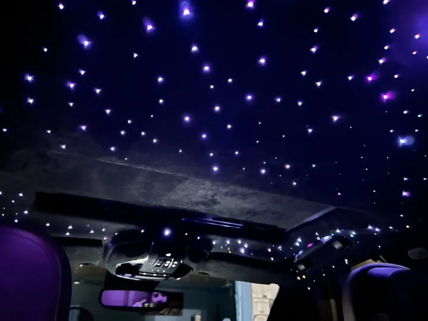 Interior car roof with starry night LED lights. Purple seats, dark setting.
