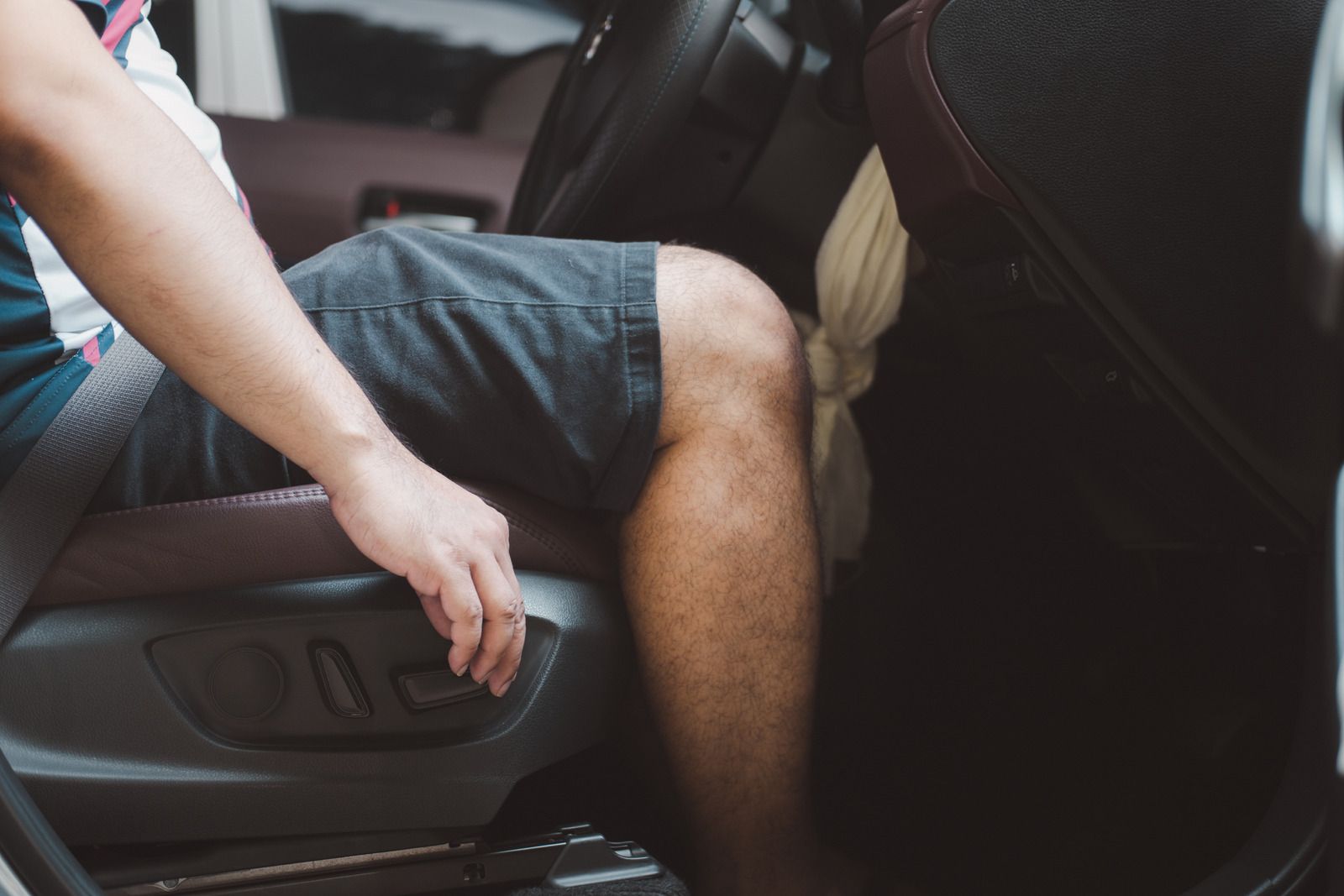 Person adjusting car seat height with hand. In car, focus on leg, seat, and control buttons.