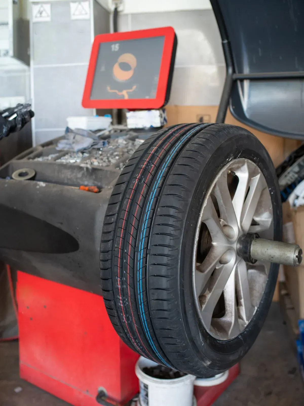 Tire on a balancing machine, red and black, in a garage.