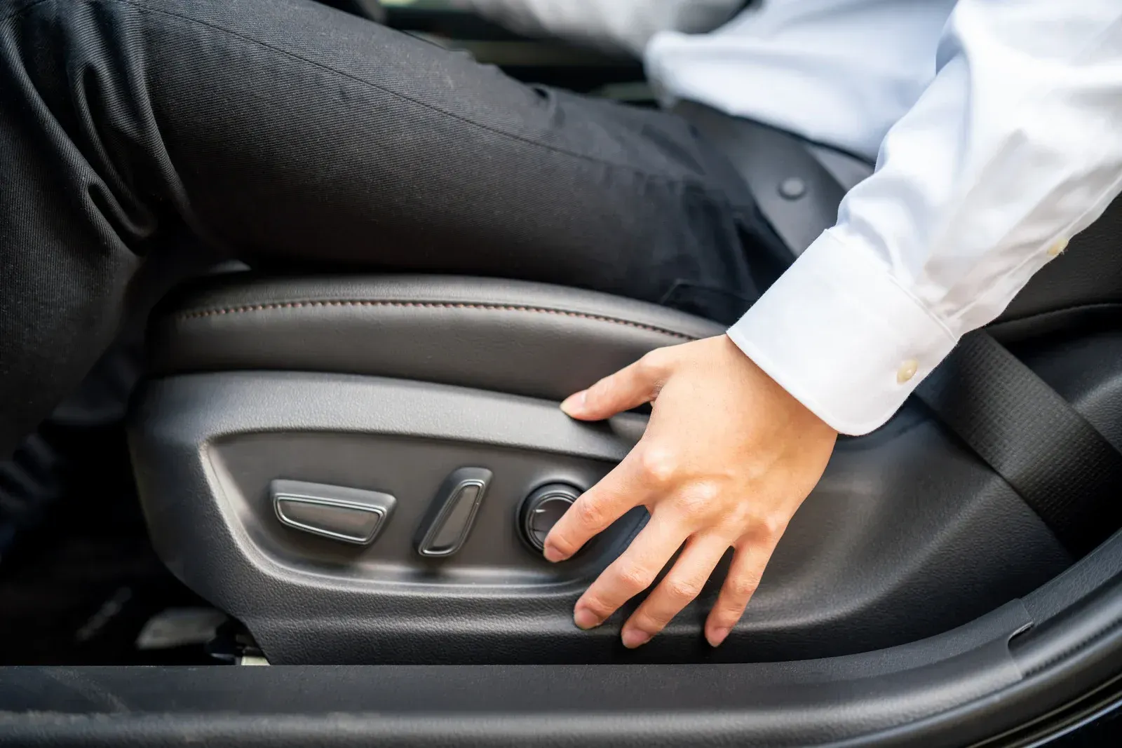 Person adjusting car seat controls with their hand.