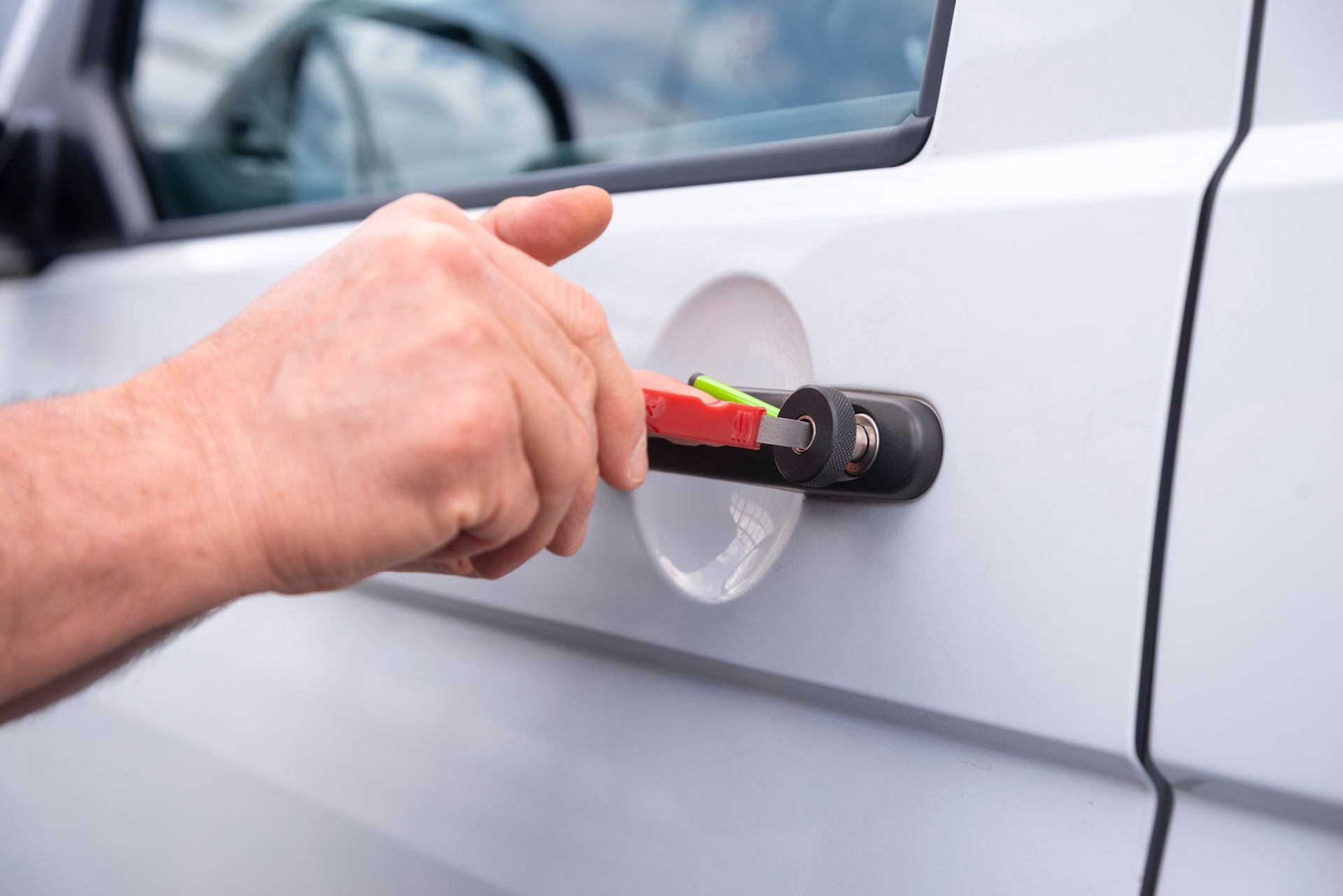A hand inserts a key with a bright red and yellow key fob into the door lock of a light-colored vehicle.