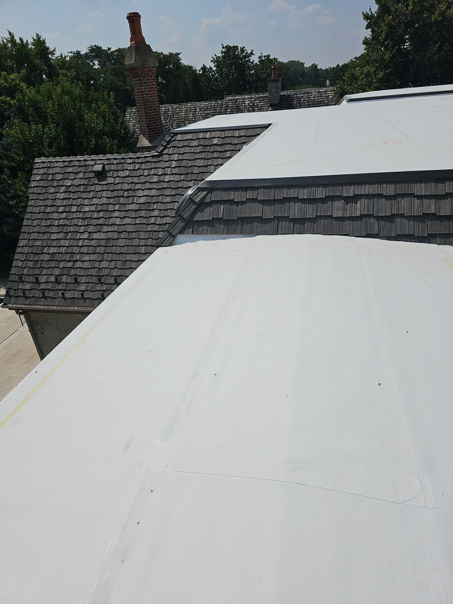 Two-story house with gray shingle roof, brick chimney, and blue trim against a bright blue sky with clouds.