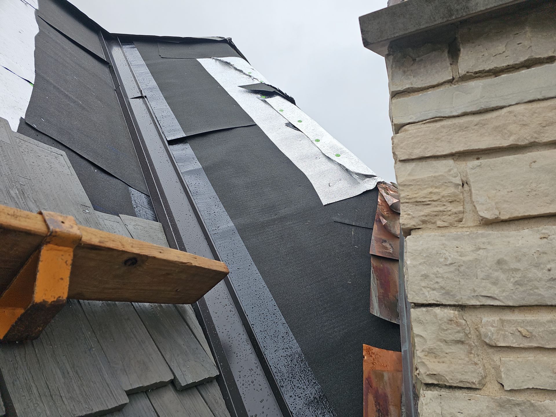 Close-up of a house with a brown roof, blue sky, and tan siding.