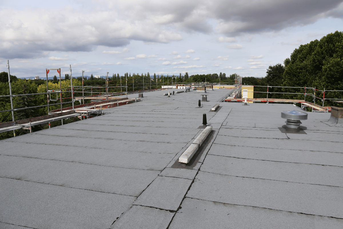 Flat gray commercial roof with vents, safety railings, and cloudy sky.