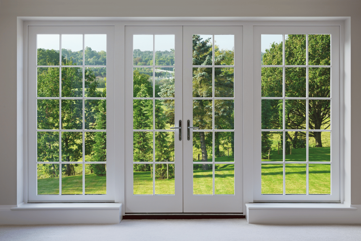 White French doors open to a vibrant green outdoor scene with trees and a grassy lawn.