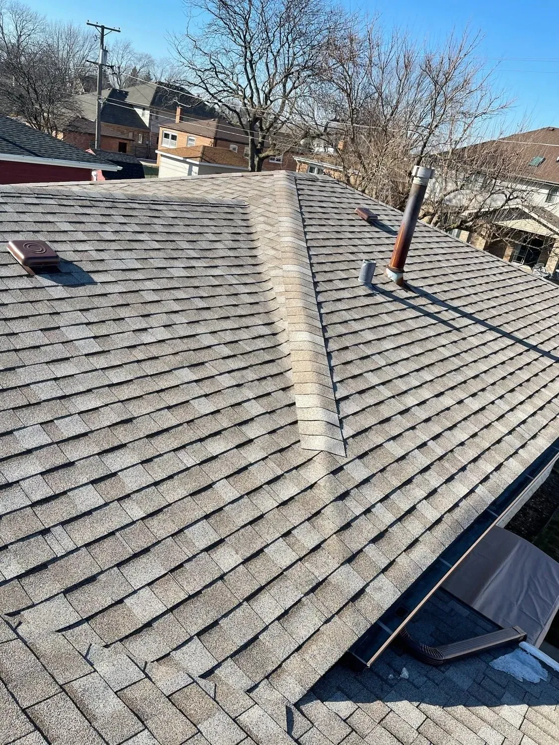Gray shingle roof with a central ridge. A chimney and some tiles are visible. Sunny day.