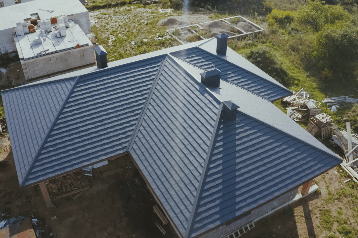 Aerial view of a blue metal roof under construction with three chimneys.