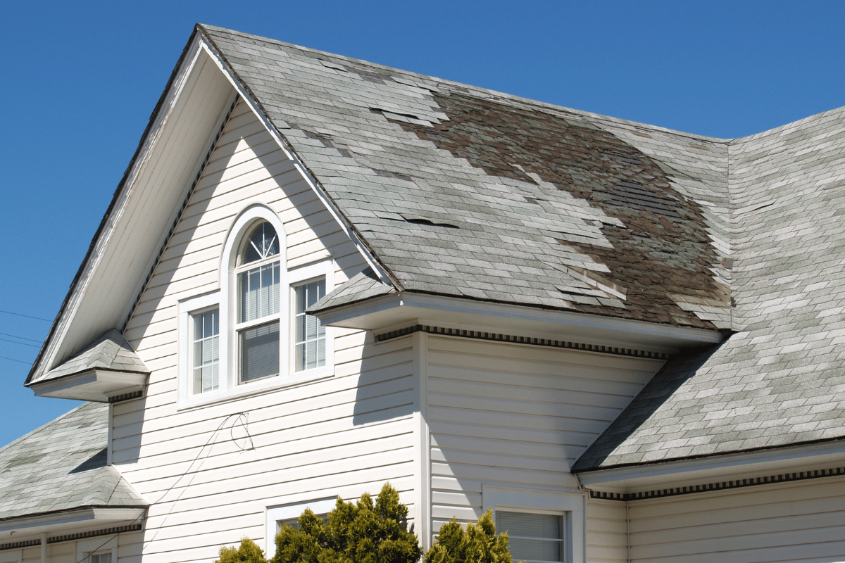 White house with a gray, algae-covered roof and arched window against a clear blue sky.
