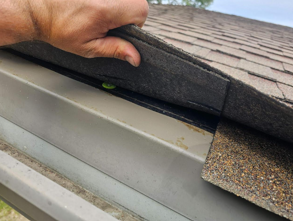 Gray shingle roof with a central ridge. A chimney and some tiles are visible. Sunny day.