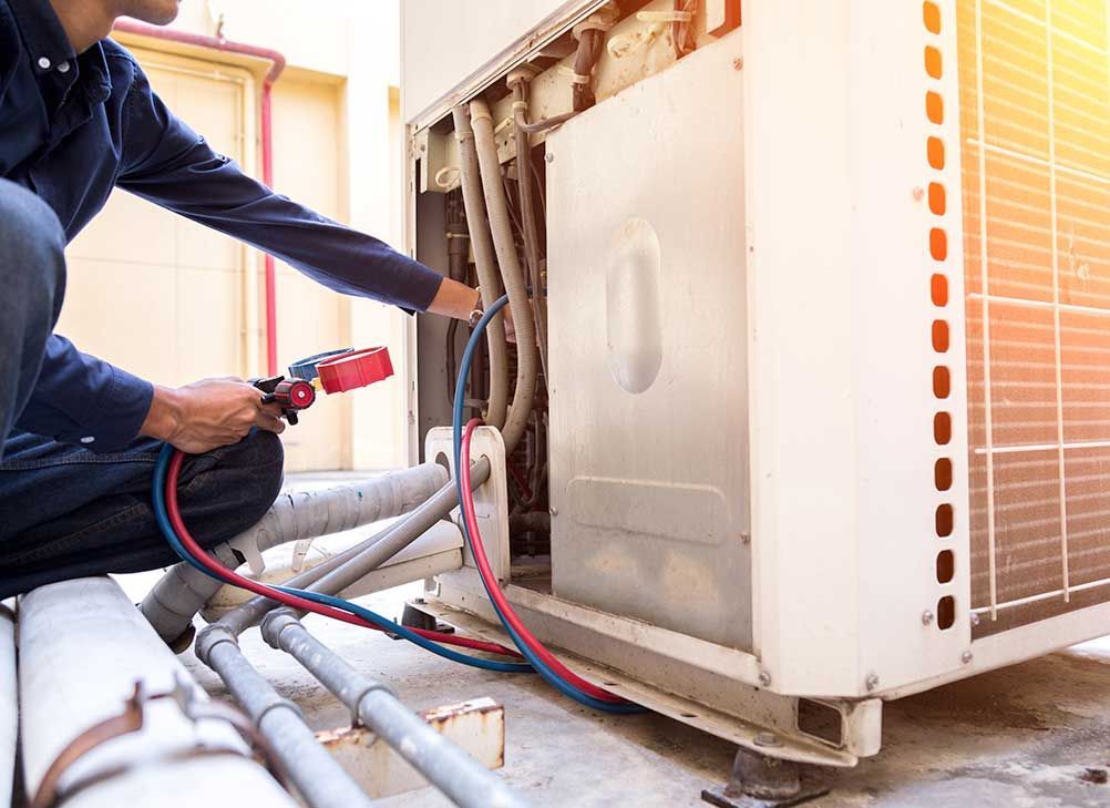 A man is working on an air conditioner with a hose.