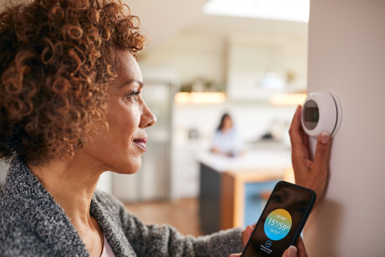 A woman is adjusting a thermostat with a smart phone.