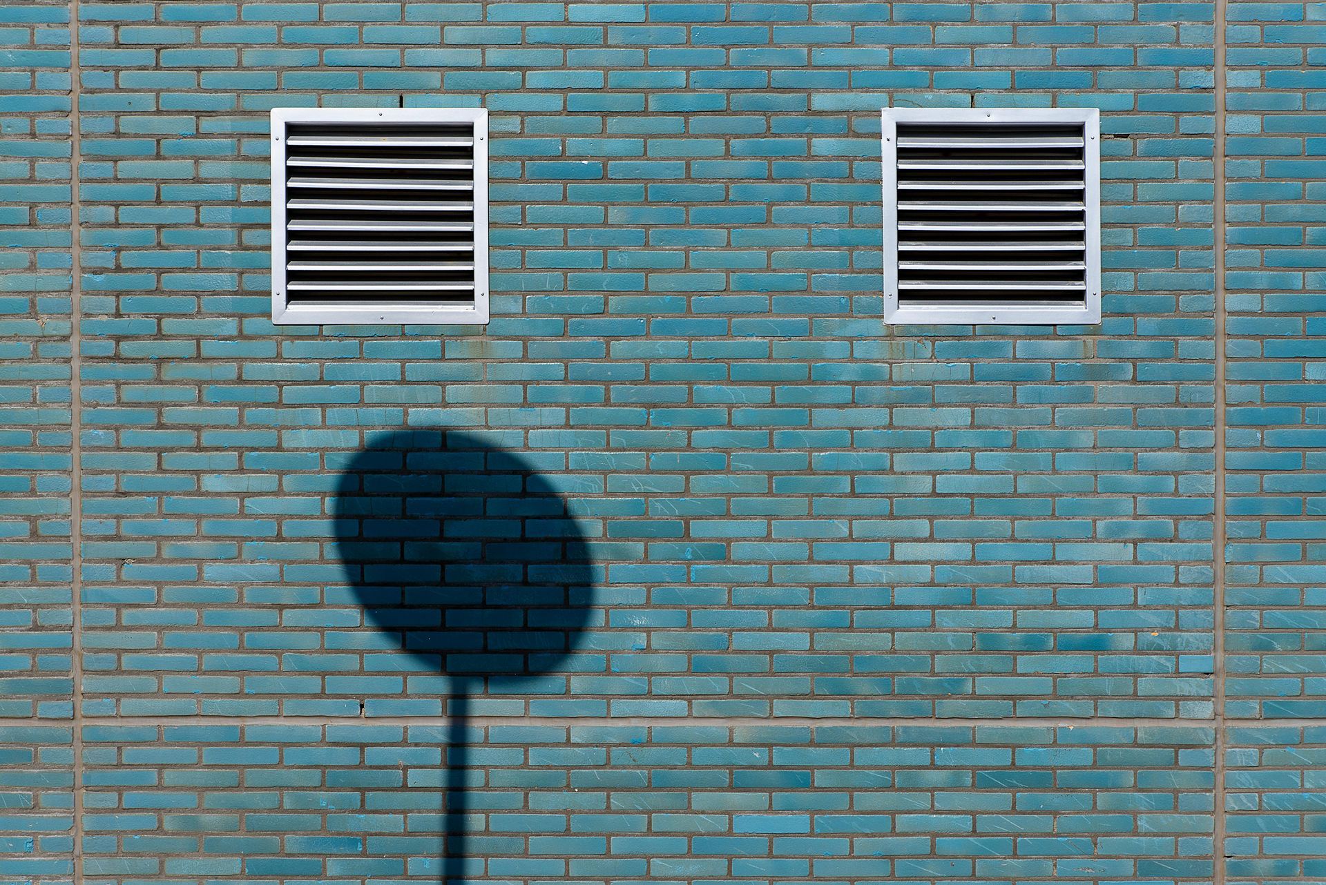 A row of stainless steel industrial clothes dryers in a laundromat, shown in a moody black and white filter.