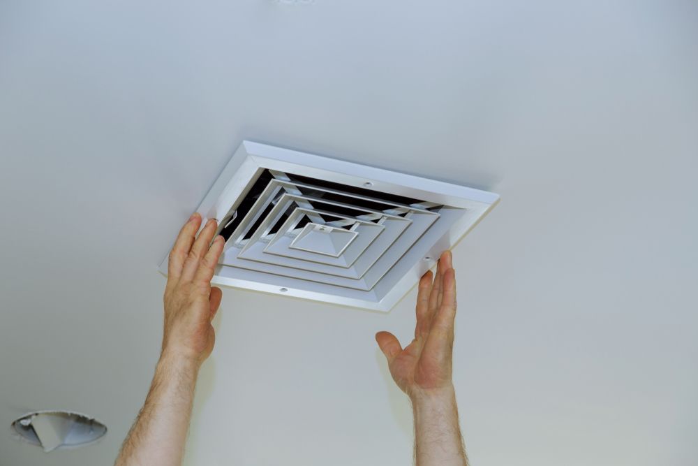 Hands installing a white air vent cover on a white ceiling.