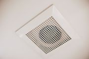 White ceiling-mounted bathroom vent with square grid and center fan, angled view.