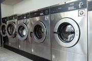 Row of silver washing machines in a laundromat, with black control panels and glass doors.